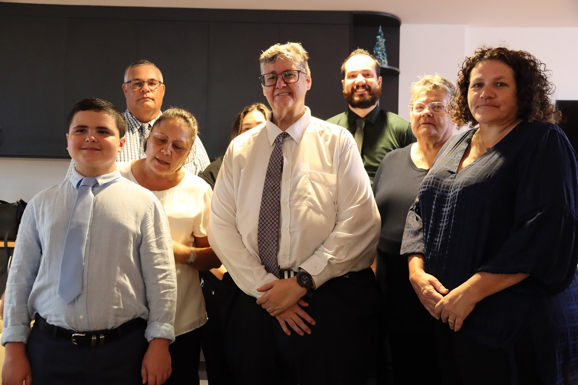 A man in a collared shirt and tie surrounded by a group of family members, all smiling.
