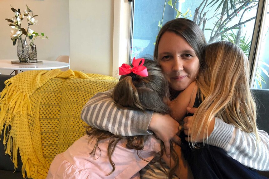 Mother cuddles two little girls on couch