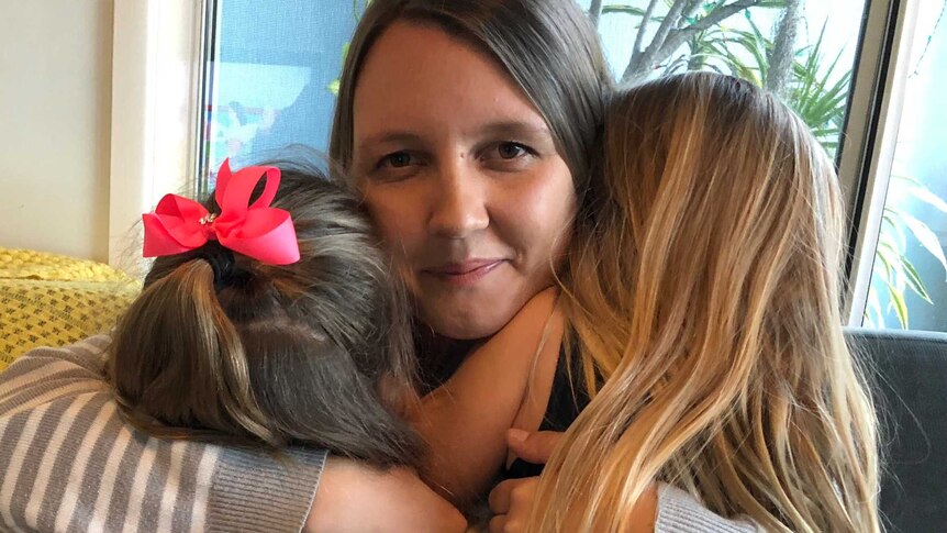 Mother cuddles two little girls on couch