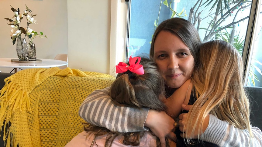 Mother cuddles two little girls on couch