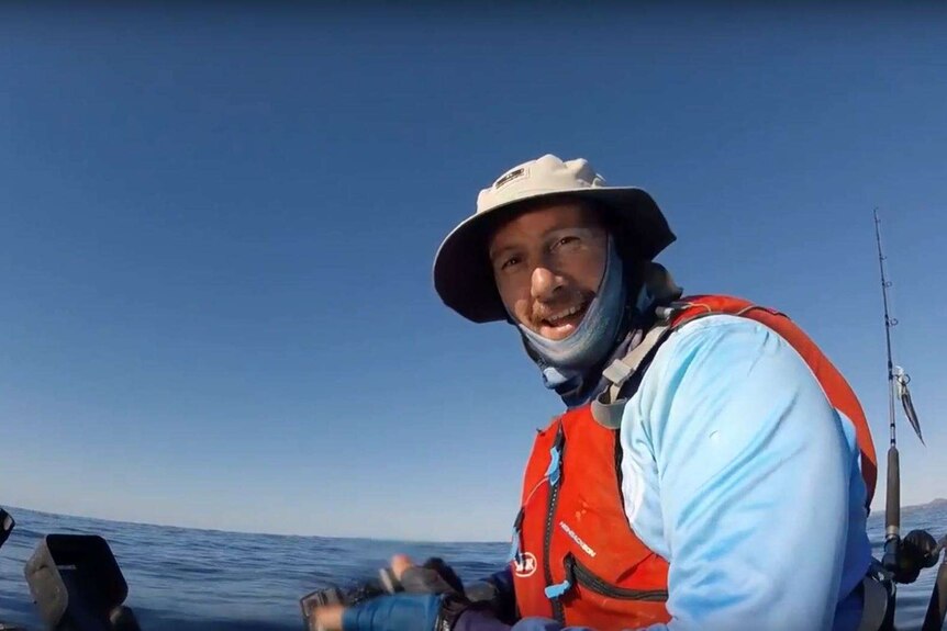 Fisherman sitting in kayak in the middle of the ocean on a sunny day smiling.