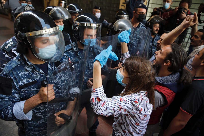 Mask wearing anti-government protesters in Lebanon clash with security forces in uniform, also wearing a mask.