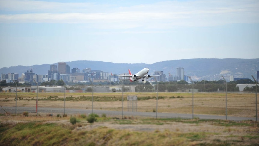 An aeroplane takes off at an airport in front of a city skyline and hills