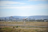 An aeroplane takes off at an airport in front of a city skyline and hills