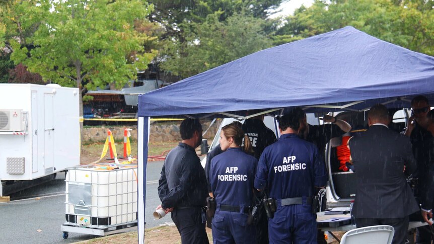 AFP forensic officers under cover, to keep out of the rain.