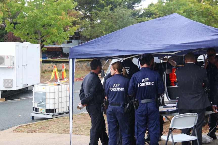 AFP forensic officers under cover, to keep out of the rain.