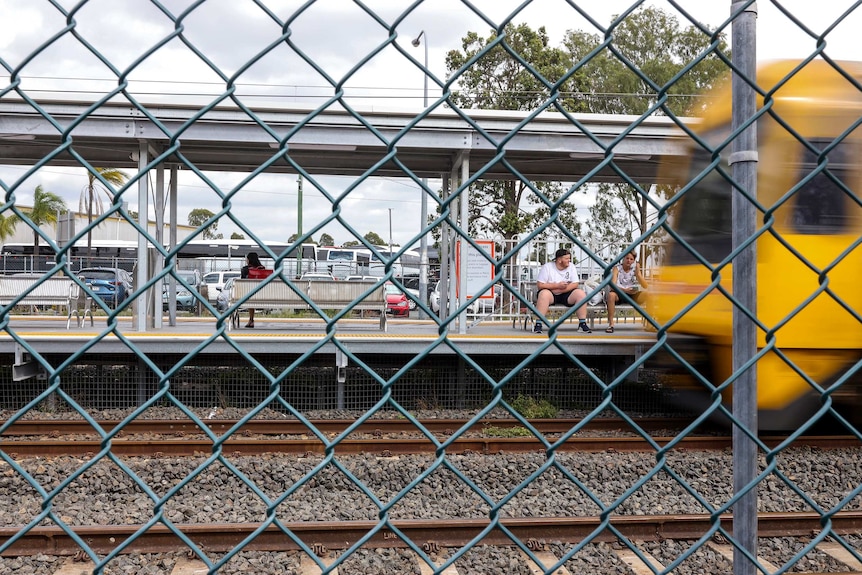 People sit waiting on the platform as a train arrives.