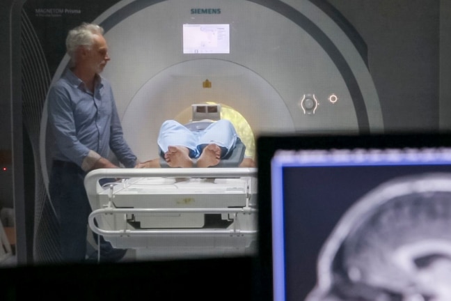 A man stands next to an MRI machine while a person gets an xray.