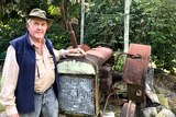 An elderly man leans against a rusty old tractor