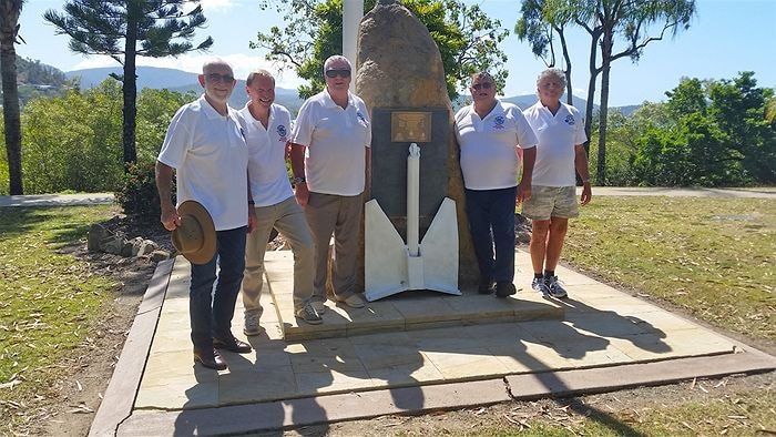 Five men stand near a memorial.