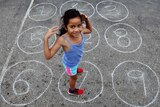 A girl stands on a netball court inside a circle drawn in chalk with the number seven written inside.