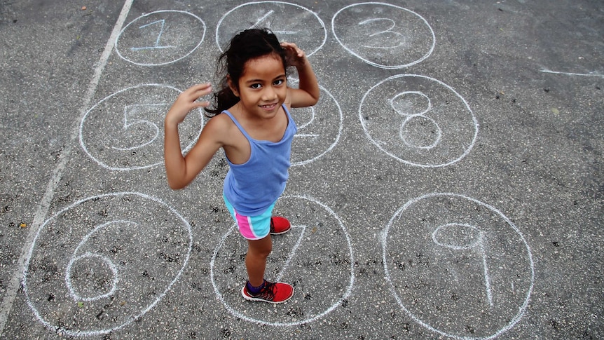 A girl stands on a netball court inside a circle drawn in chalk with the number seven written inside.