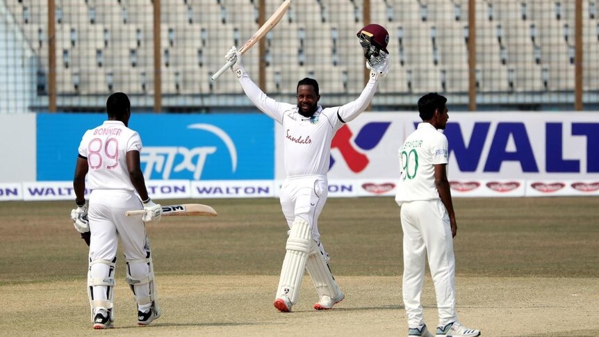 West Indies batsman Kyle Mayers raises his bat and helmet after a century in a Test against Bangladesh.