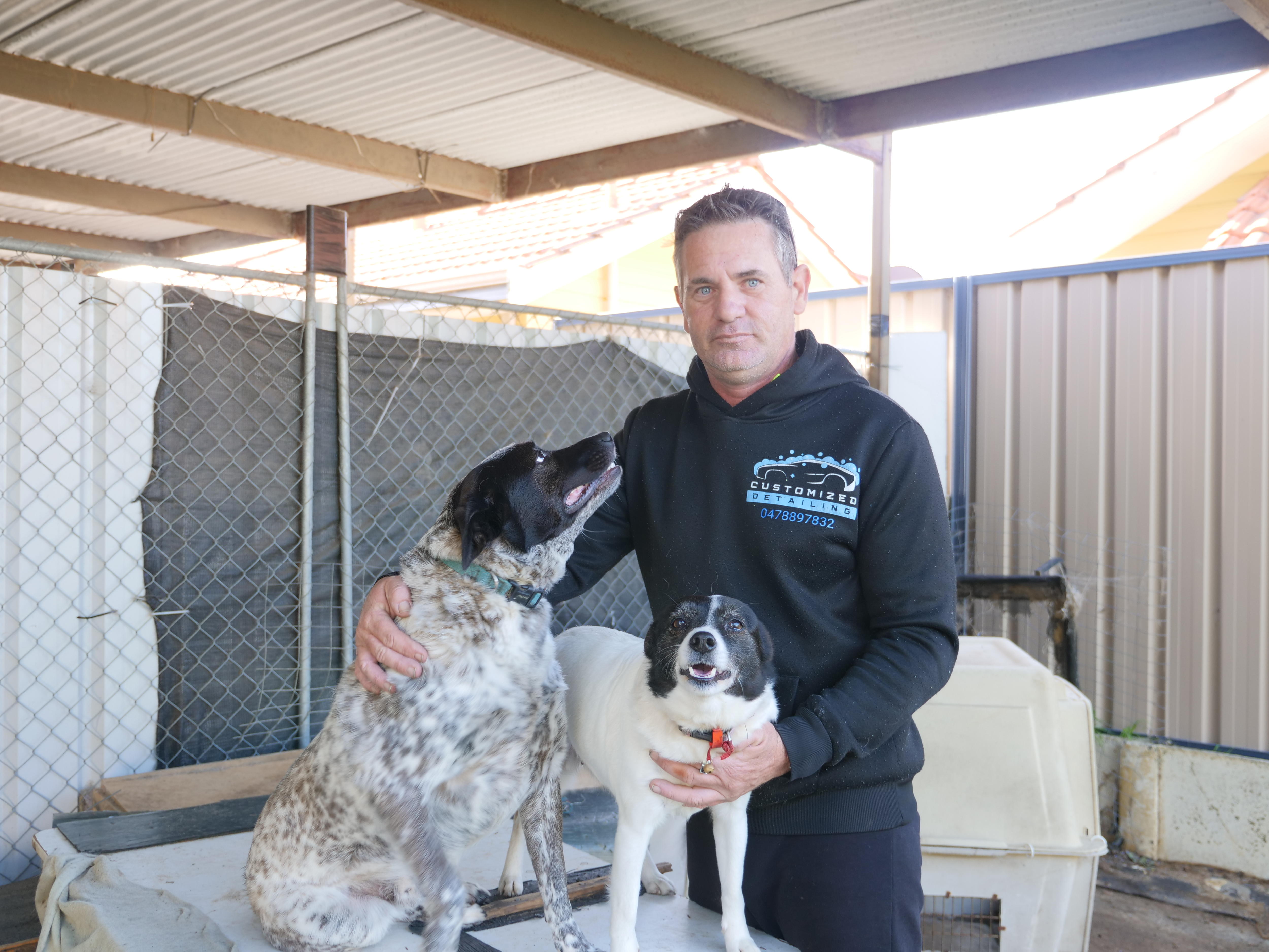 A man with his arms around two dogs