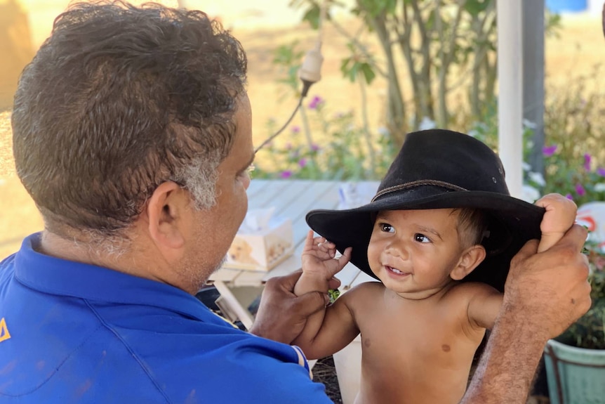 A baby, wearing a black hat, smiles at a man.