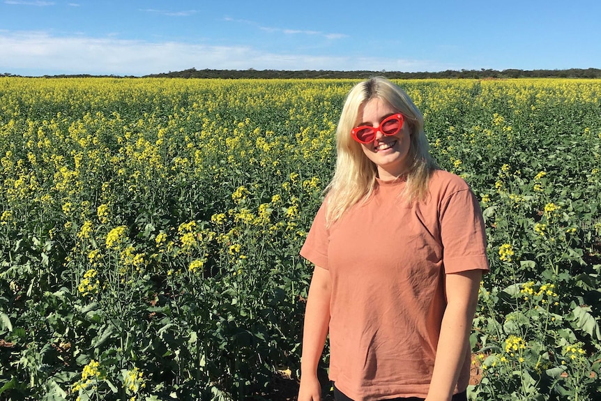 A girl with bright red sunnies stands in front of a vibrant yellow canola crop