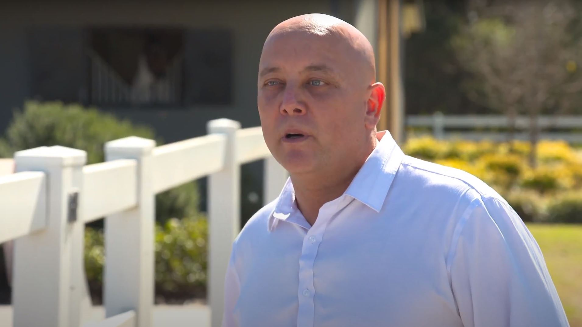 A screenshot from a video showing a bald man in a white shirt speaking to camera.