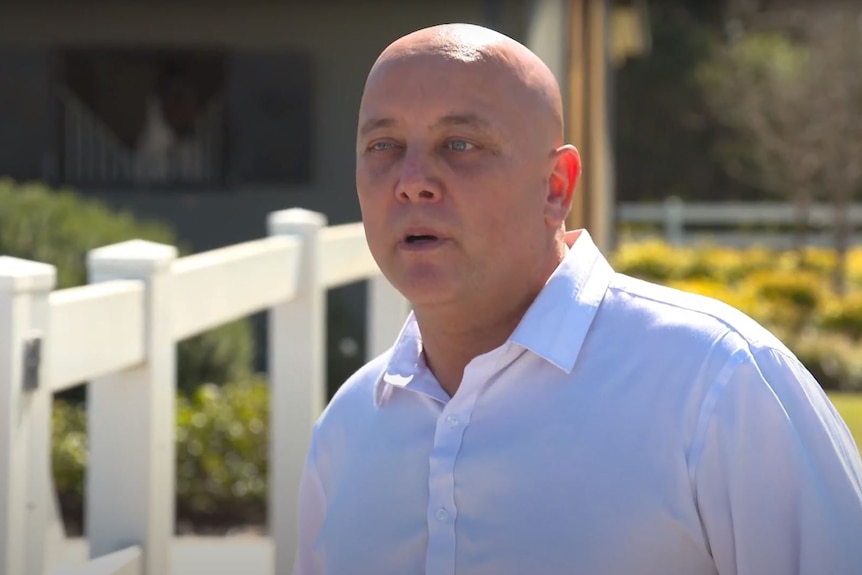 A screenshot from a video showing a bald man in a white shirt speaking to camera.