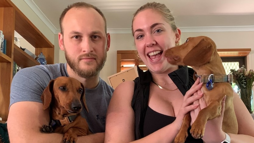 A man and woman smile while holding two dachshunds. 