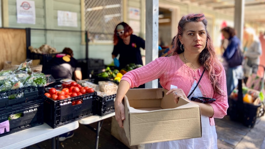 a woman holding onto an empty cardboard box outside a food charity