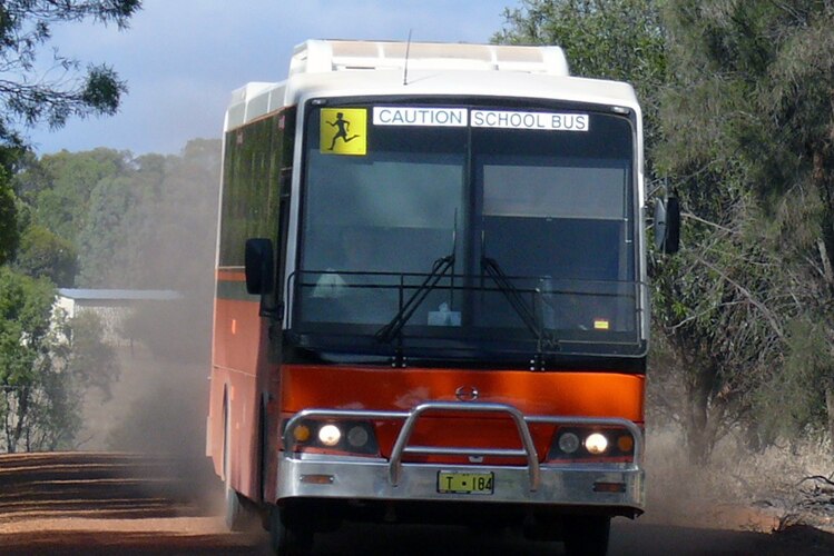 An orange school bus drives on a gravel road in Western Australia.