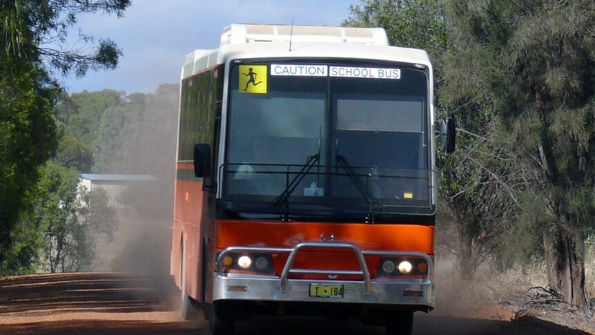 An orange school bus drives on a gravel road in Western Australia.
