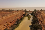 A narrow, muddy river flowing through dry, red earth