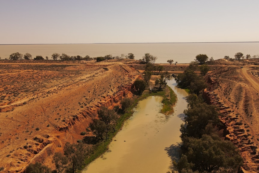 A channel of water between tree-lined red earth.