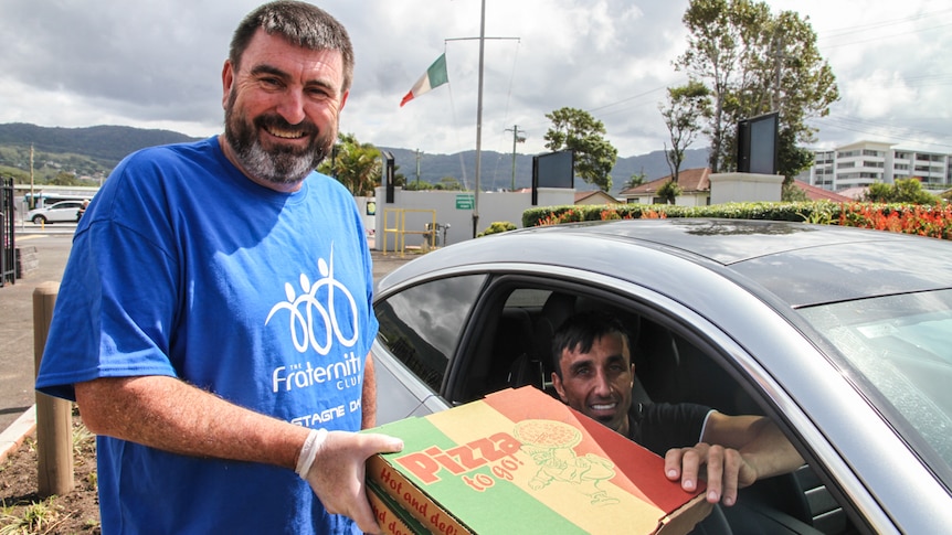 A man, wearing latex gloves, delivers pizza to another man in a car