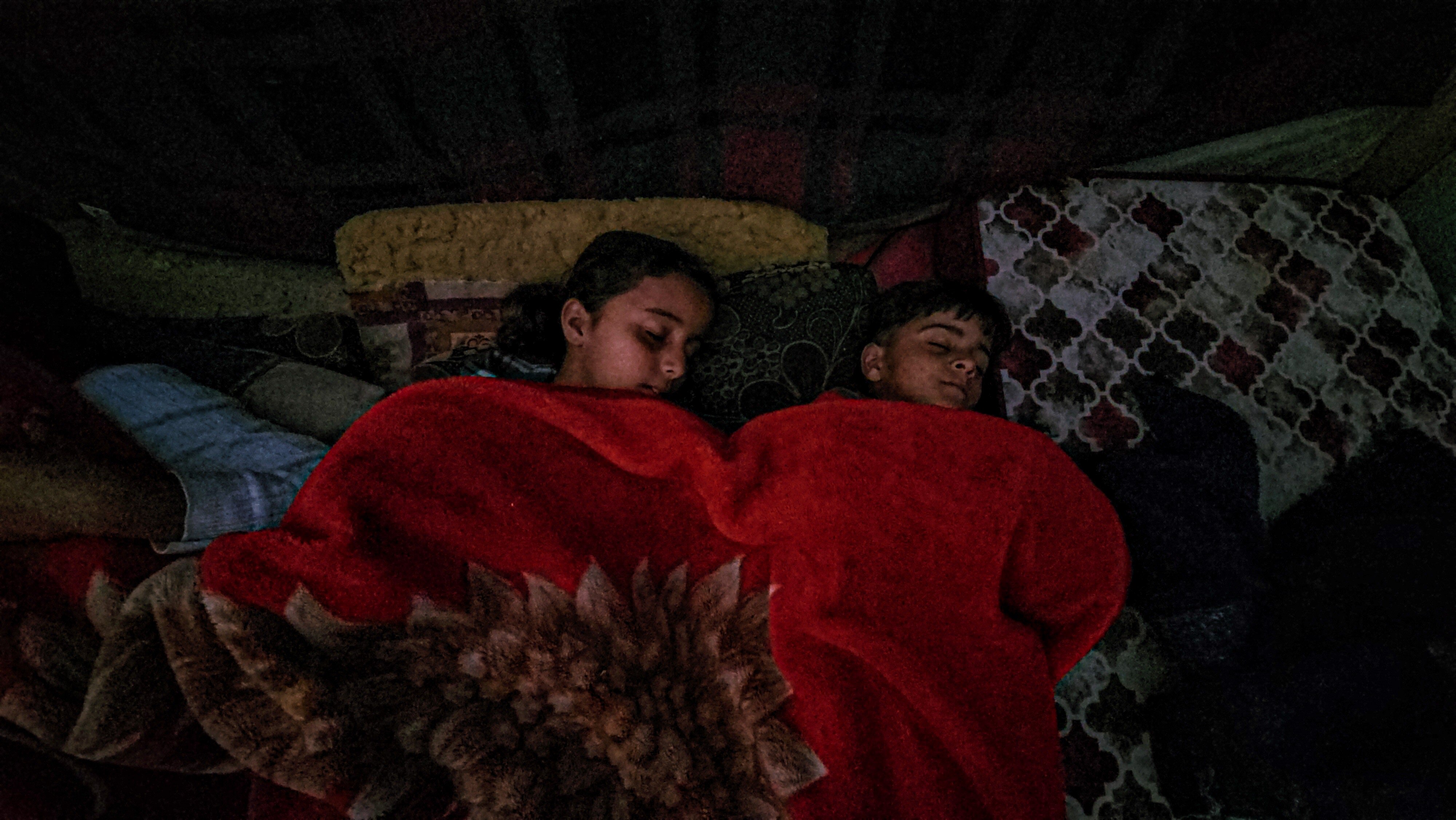 Two children asleep under a red blanket 