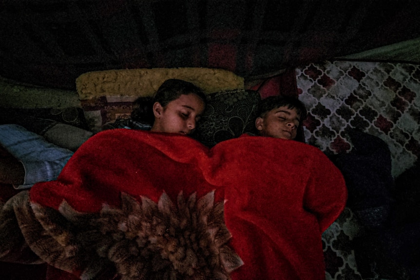 Two children asleep under a red blanket 