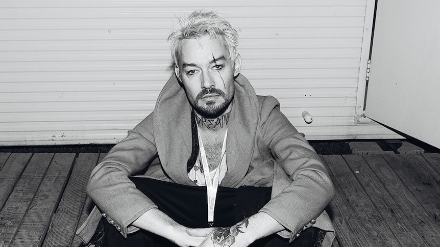 A black and white photograph of Daniel Johns sitting on the ground.