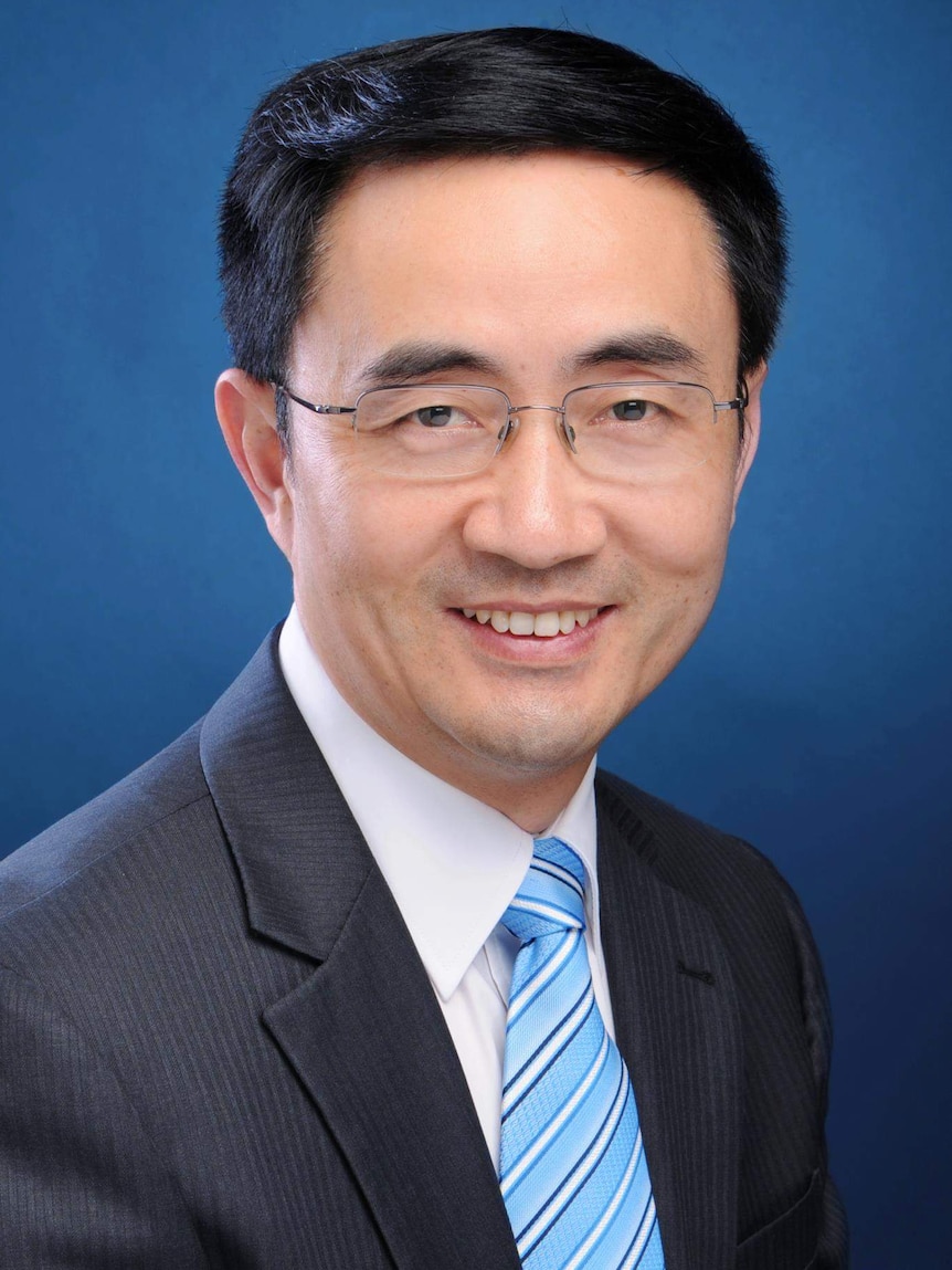 A promotional headshot shows Jian Yang wearing a grey suit, blue striped tie and glasses. He is in front of a blue background.