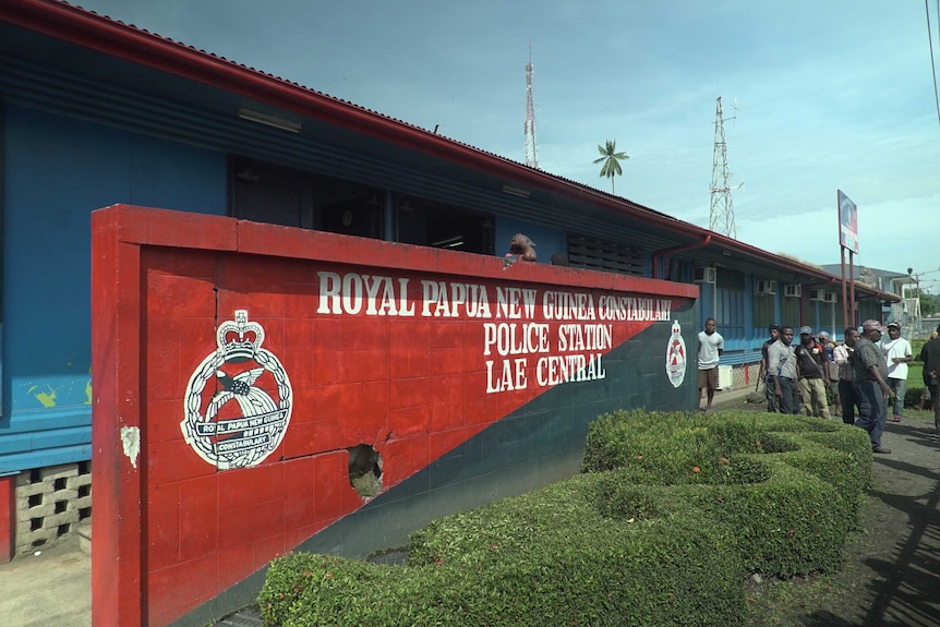 The front of the Lae Police Station with red and black signage painted on a brick wall at the front of the lowset building