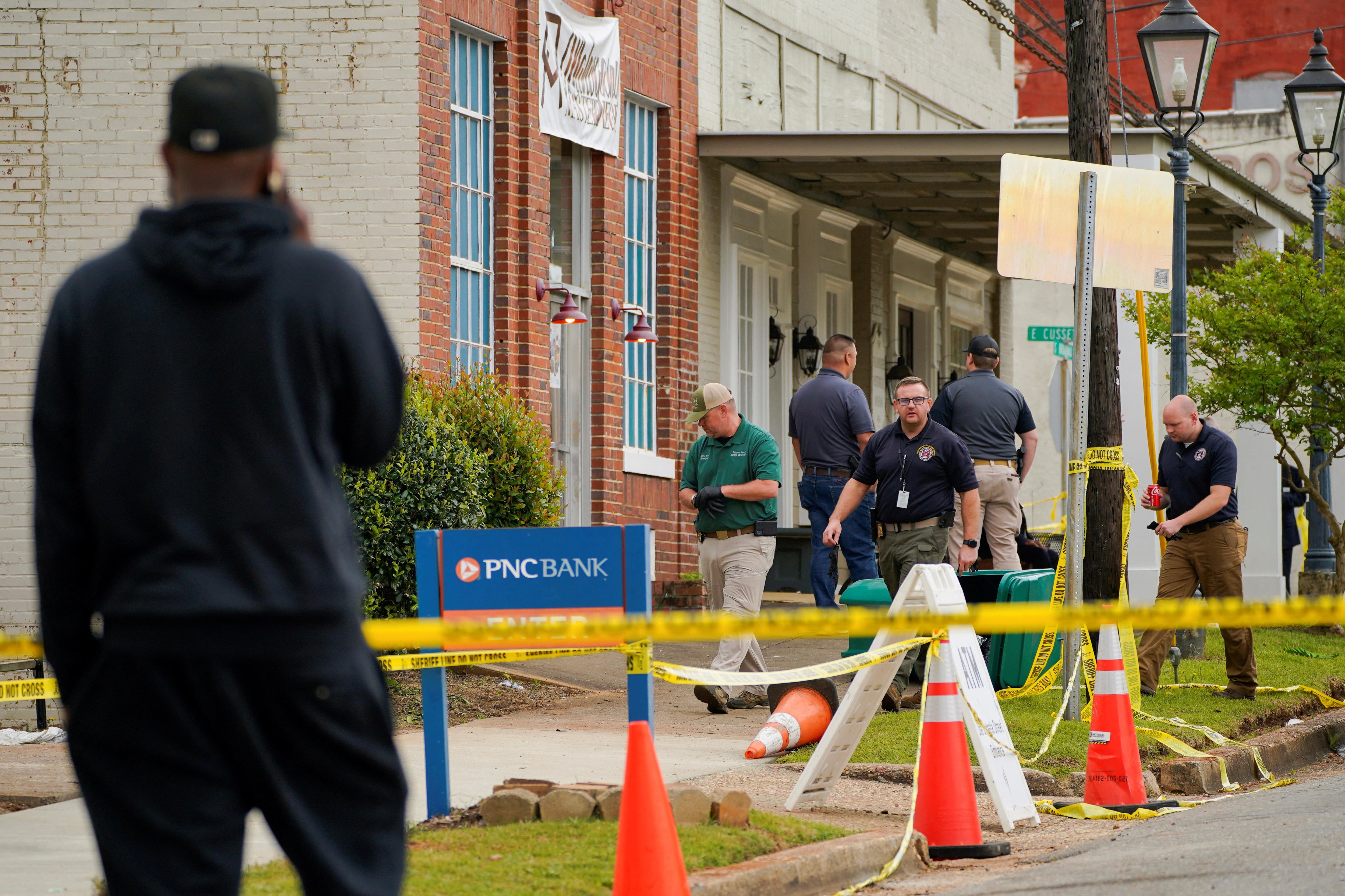 A man watches five investigators cordon off a crime scene on a pavement outside a building.