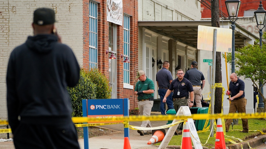 A man watches five investigators cordon off a crime scene on a pavement outside a building.