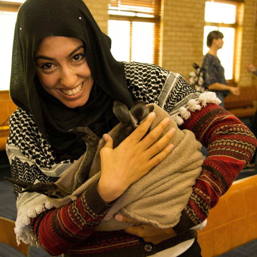 Aseel looks excited, holding a kangaroo joey in a sack.