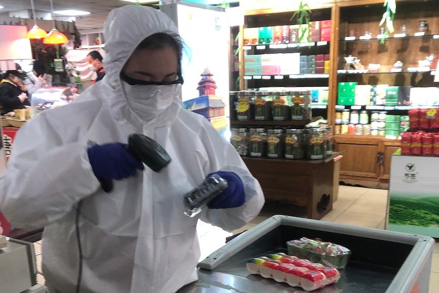A supermarket worker scanning items dressed in protective clothing