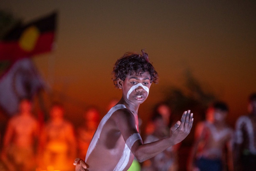 A young Indigenous boy with traditional paint dances.