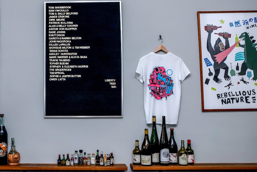 Wall of a bar with three signs on the wall with text and a row of wine bottles on shelf 