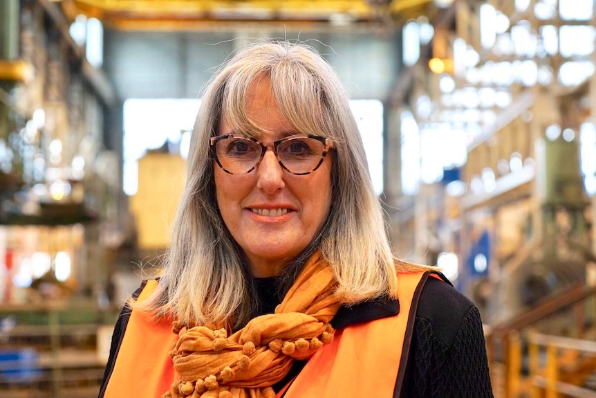 Margaret O'Rourke wears a bright orange scarf and high-vis orange vest, she has glasses and grey hair.