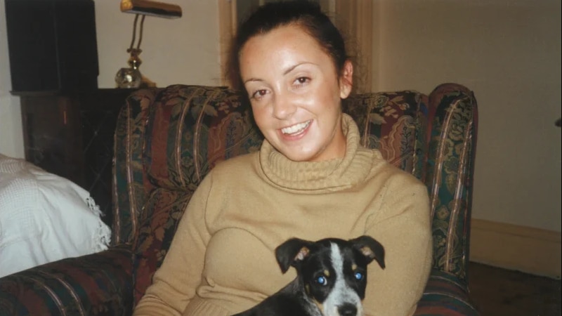 Annie O'Brien smiles, sitting on a couch holding her dog.