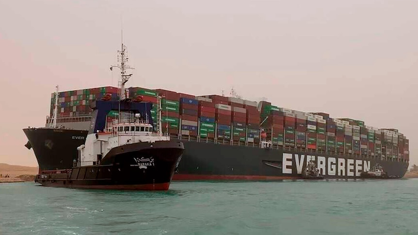 A boat navigates in front of a massive cargo ship, named the Ever Green,