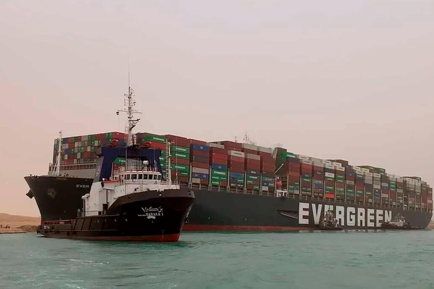 A boat navigates in front of a massive cargo ship, named the Ever Green,