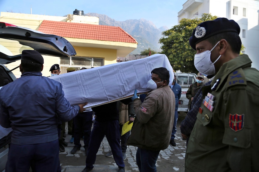 Health workers carry the coffin of a victim into a vehicle.