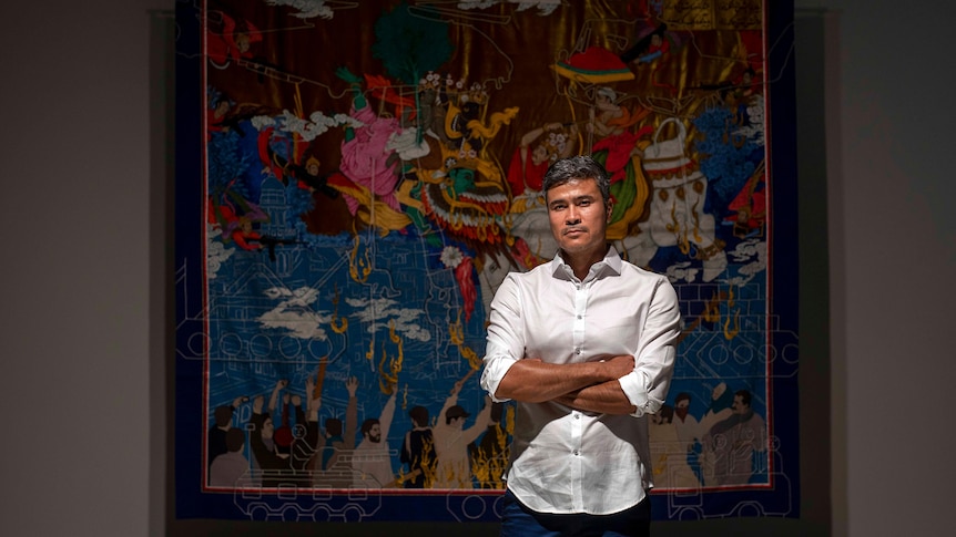 Artist Khadim Ali standing in front of one his ornate tapestries