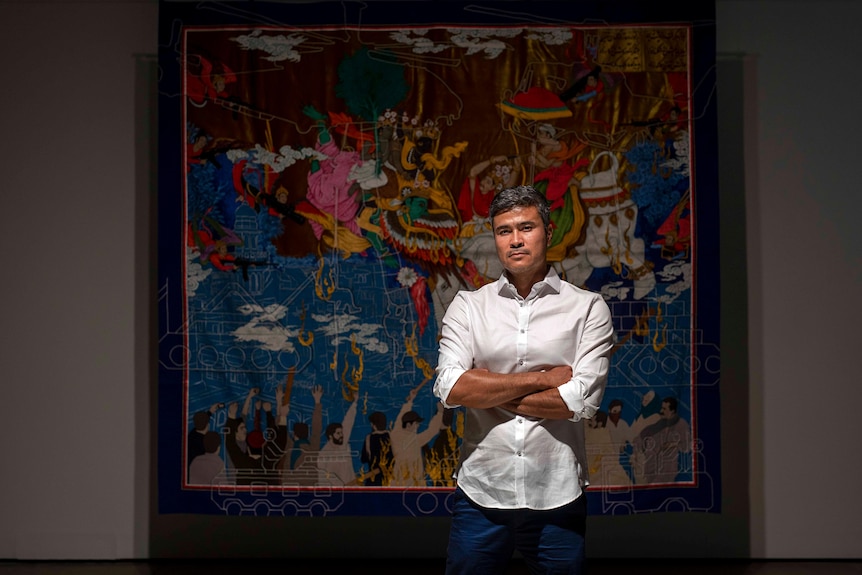 Artist Khadim Ali standing in front of one his ornate tapestries