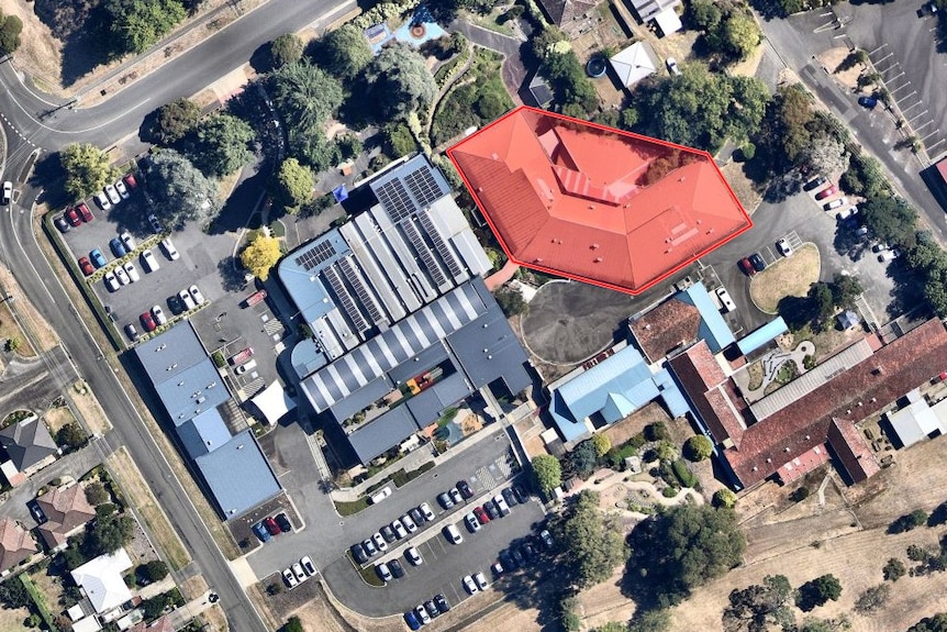 An aerial view of several large buildings and some car parks, with one building highlighted in red.