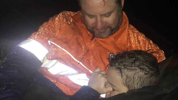 A weary man and a boy, soaking wet from rain, hug during the floods in Townsville.