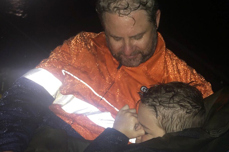 A weary man and a boy, soaking wet from rain, hug during the floods in Townsville.